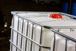 Close-up of an IBC container with a red cap, surrounded by a metal cage, used for industrial liquid storage and transport.